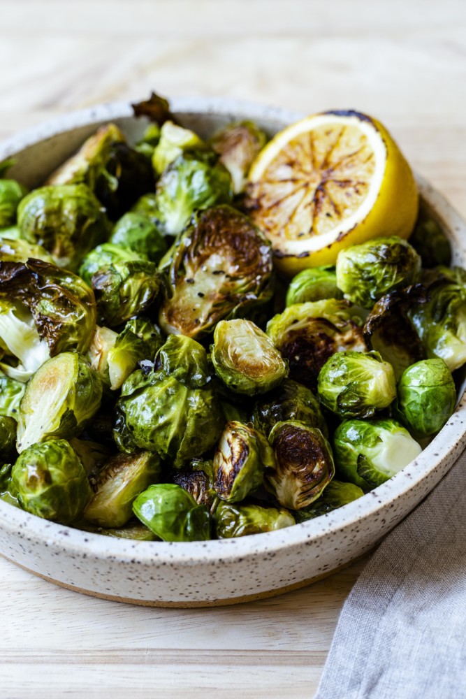 A speckled bowl full of roasted brussels sprouts and one roasted lemon half