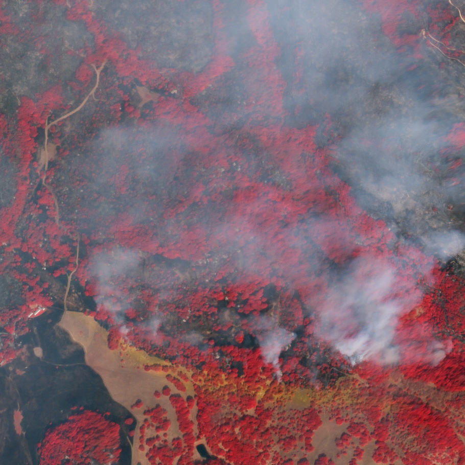 A false-color composite including near-infrared light reveals burns scars (dark gray) and unburned woodland (bright red) under the smoke. Flame retardant is red in true color, and orange in false-color.