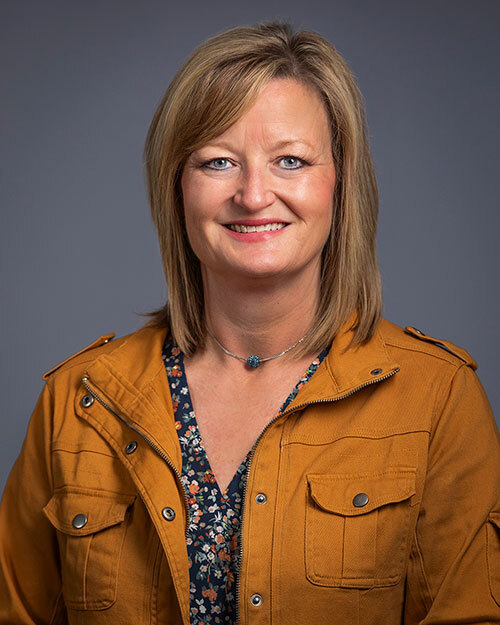 Photo of woman with blonde hair smiling wearing a yellow jacket and a floral patterned shirt