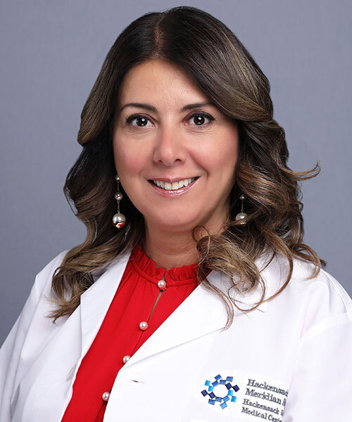Photo of woman with dark brown hair smiling and wearing a white lab coat and red shirt