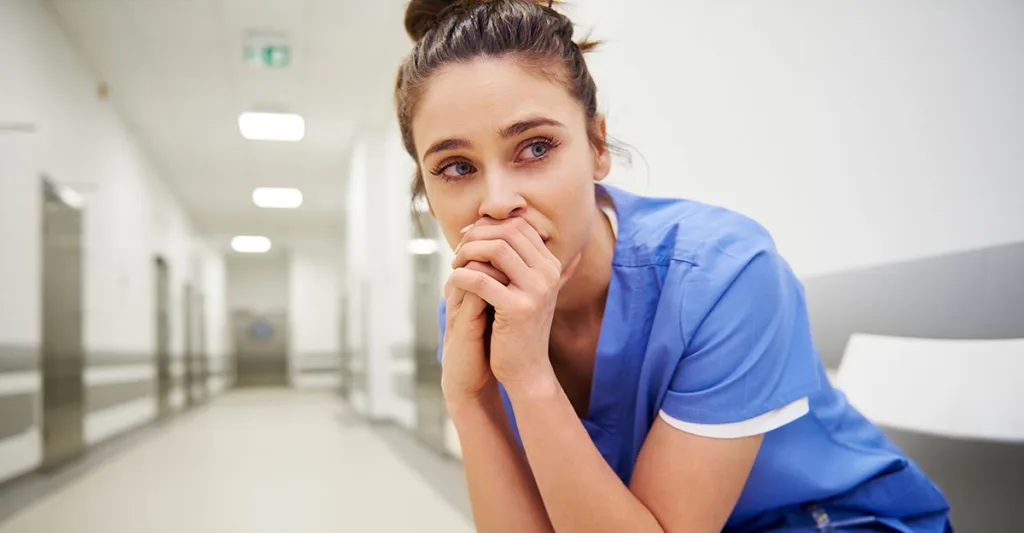 Nurse crouched in a hospital hallway with a distressed look on her face