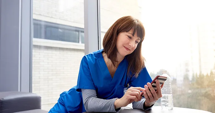 A nurse in blue scrubs smiling at her phone while she uses social media at work