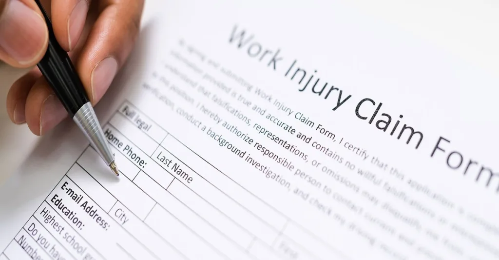 A person sing a ball point pen to fill out a form titles Work Injury Claim Form