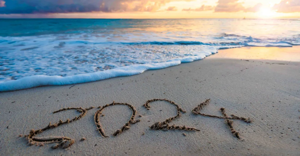 An image of a beach at sunrise with 2024 written in the sand