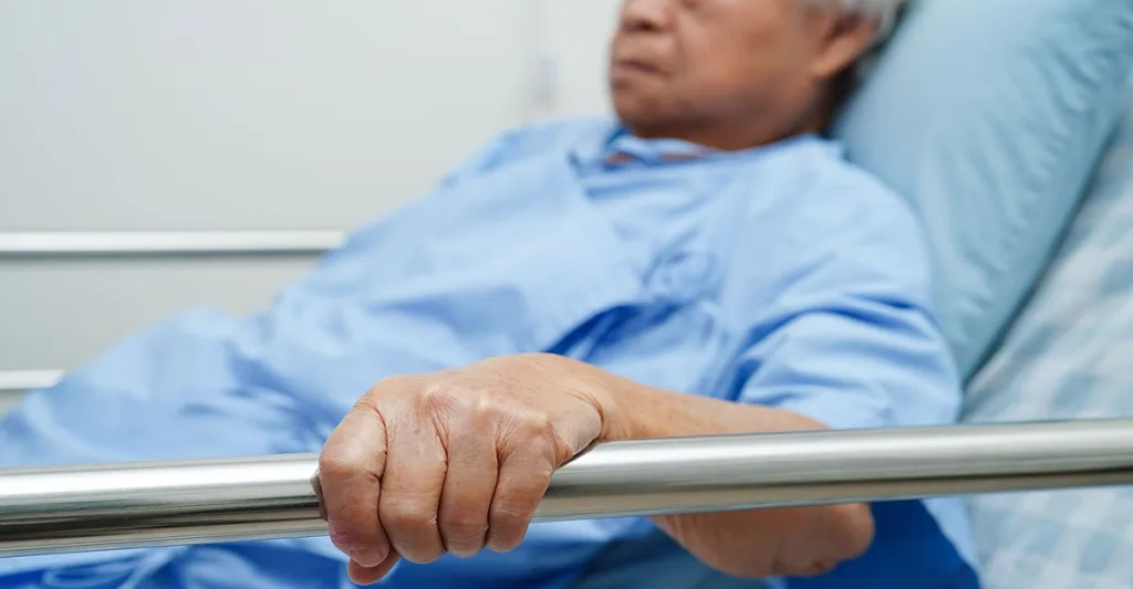 An older male lying in a hospital bed wearing a hospital gown