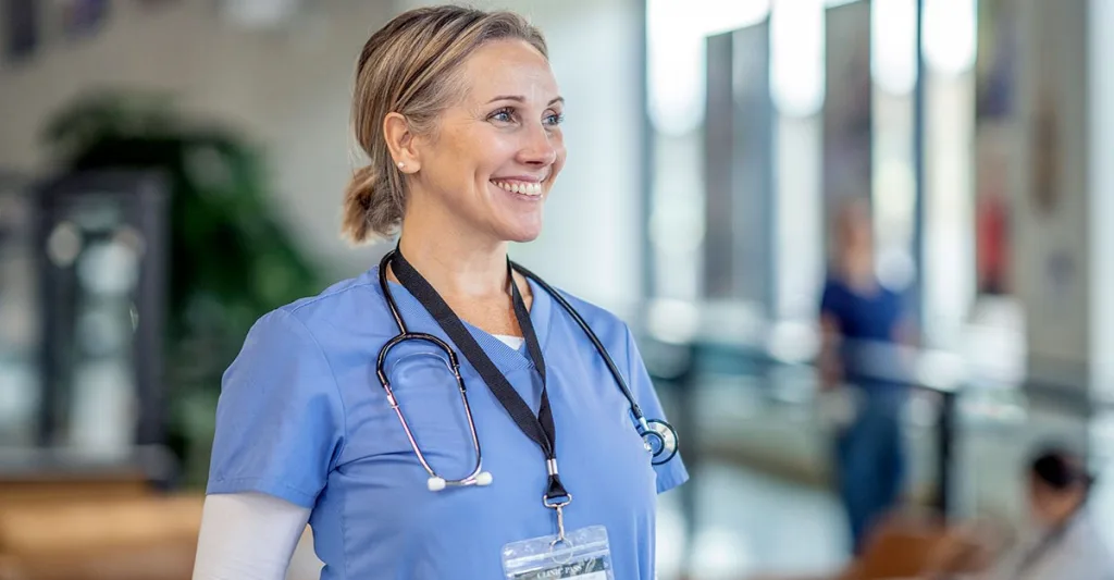 A very happy nurse smiling while looking off camera standing in a hospital waiting room