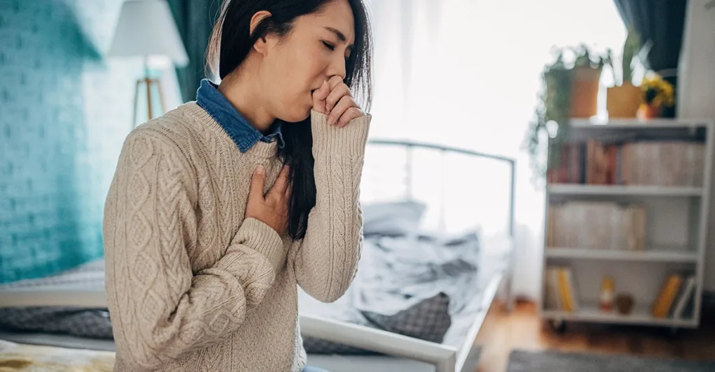 Woman coughing with her hand covering her mouth and her other hand on her heart