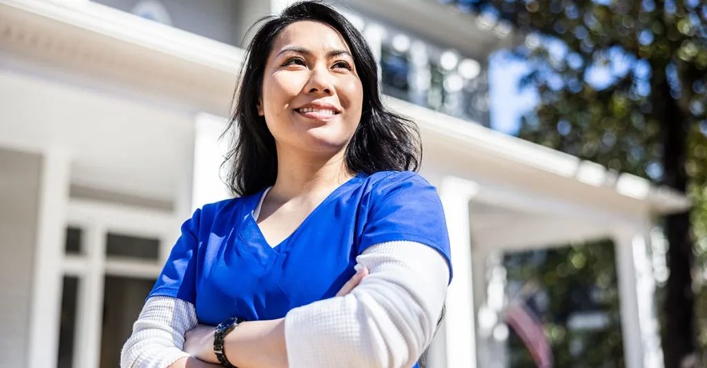 Nurse in blue scrubs standing outside with arms crossed