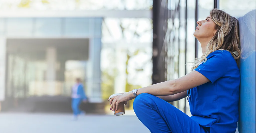 Nurse burnout - stressed nurse sitting against a wall