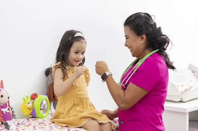 Pediatric nurse practices play techniques with young patient by giving her a fistbump.