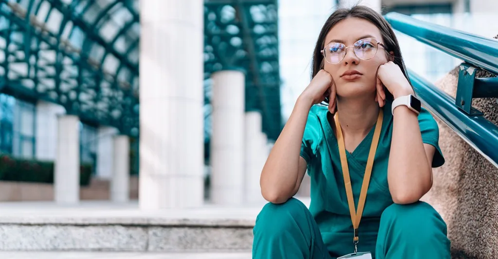 Nurse sitting on steps experiencing nurse burnout symptoms