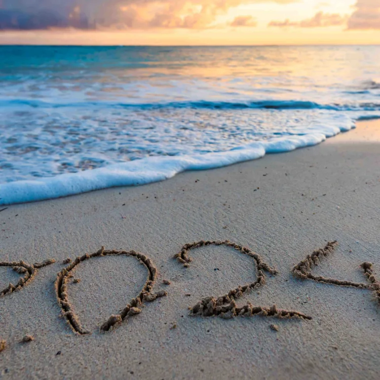 An image of a beach at sunrise with 2024 written in the sand