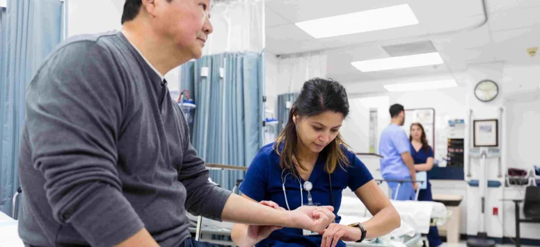 Nurse in emergency department taking a patients pulse while they sit on a bed