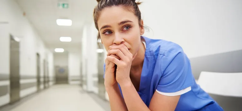 Nurse crouched in a hospital hallway with a distressed look on her face
