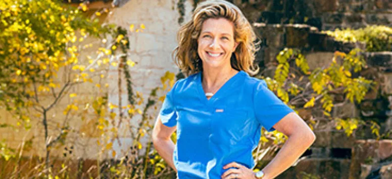 A nurse in blue scrubs standing in a backyard while the sun is shining brightly