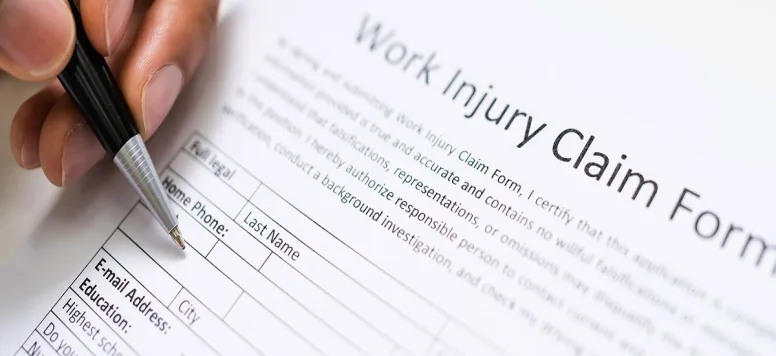 A person sing a ball point pen to fill out a form titles Work Injury Claim Form