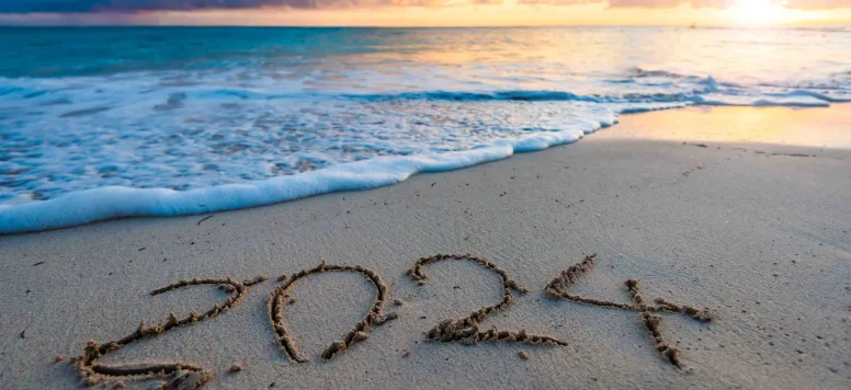 An image of a beach at sunrise with 2024 written in the sand