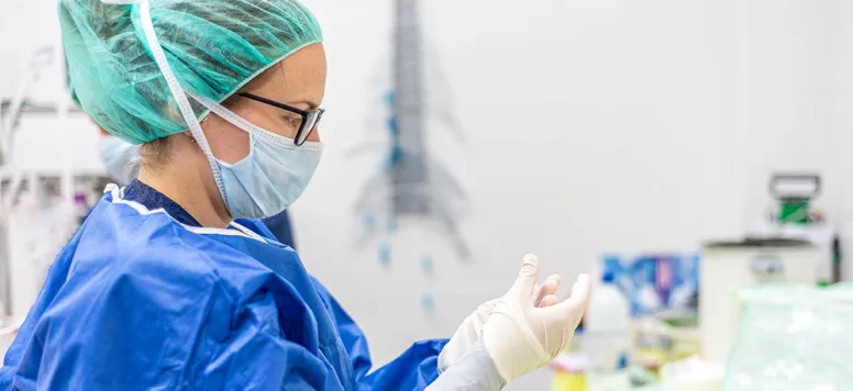 A nurse in blue scrubs and full surgical protective gear prepares for an operation