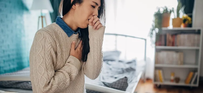 Woman coughing with her hand covering her mouth and her other hand on her heart