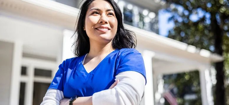 Nurse in blue scrubs standing outside with arms crossed