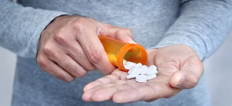 Man pouring white pills out of a prescription medication bottle and into his hand.