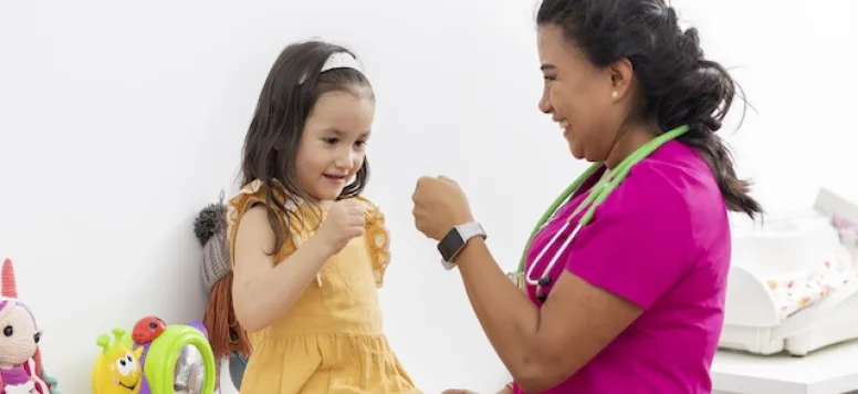 Pediatric nurse practices play techniques with young patient by giving her a fistbump.