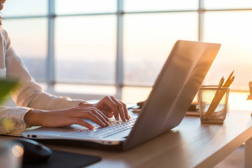 Someone typing on a laptop near the windows