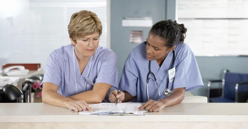 Two nurses looking over paperwork at nurses station
