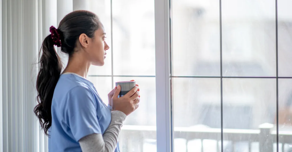 Nurse looking out the window with coffee in hand