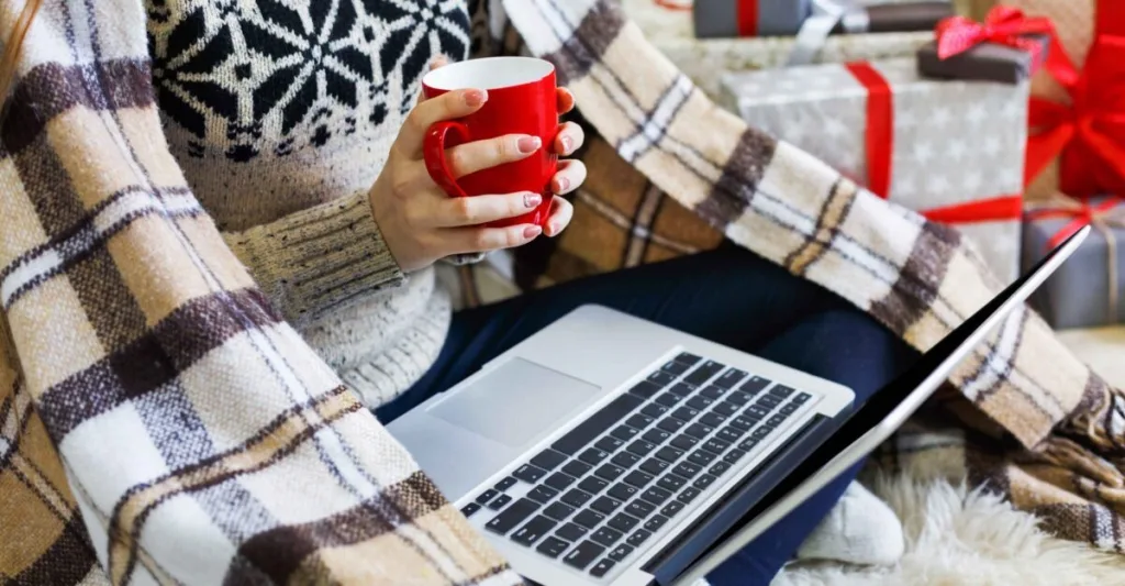 Someone on a laptop, wrapped in a blanket, holding a cup of tea