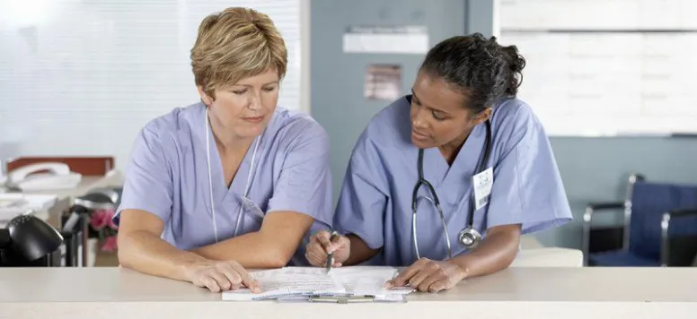 Two nurses looking over paperwork at nurses station