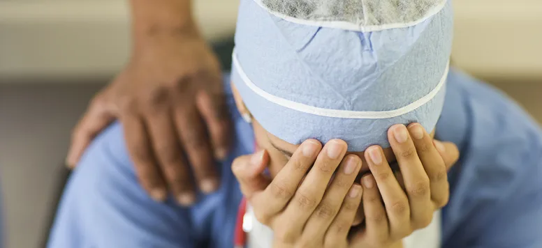 Nurse with scrub cap being consoled