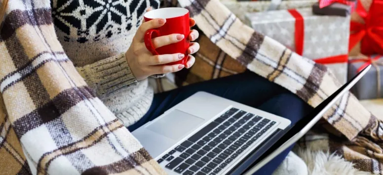 Someone on a laptop, wrapped in a blanket, holding a cup of tea