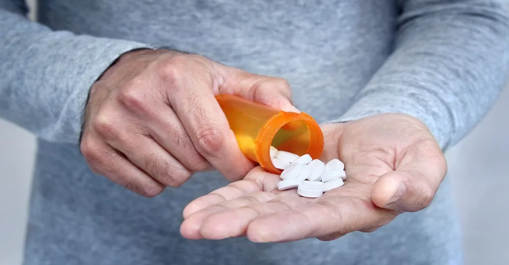 Man pouring white pills out of a prescription medication bottle and into his hand.