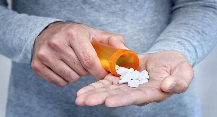 Man pouring white pills out of a prescription medication bottle and into his hand.