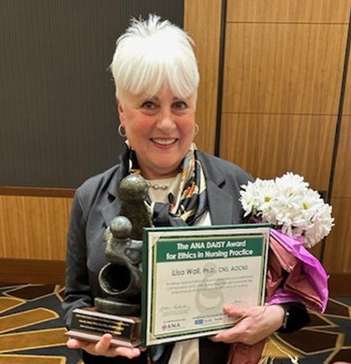 Photo of woman who is a Daisy Award winner holding award, certificate, and flowers