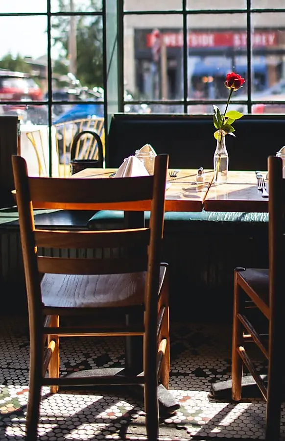 Empty wooden chair in San Jose restaurant. View of table facing window, rose in glass on table next to folded cloth.
