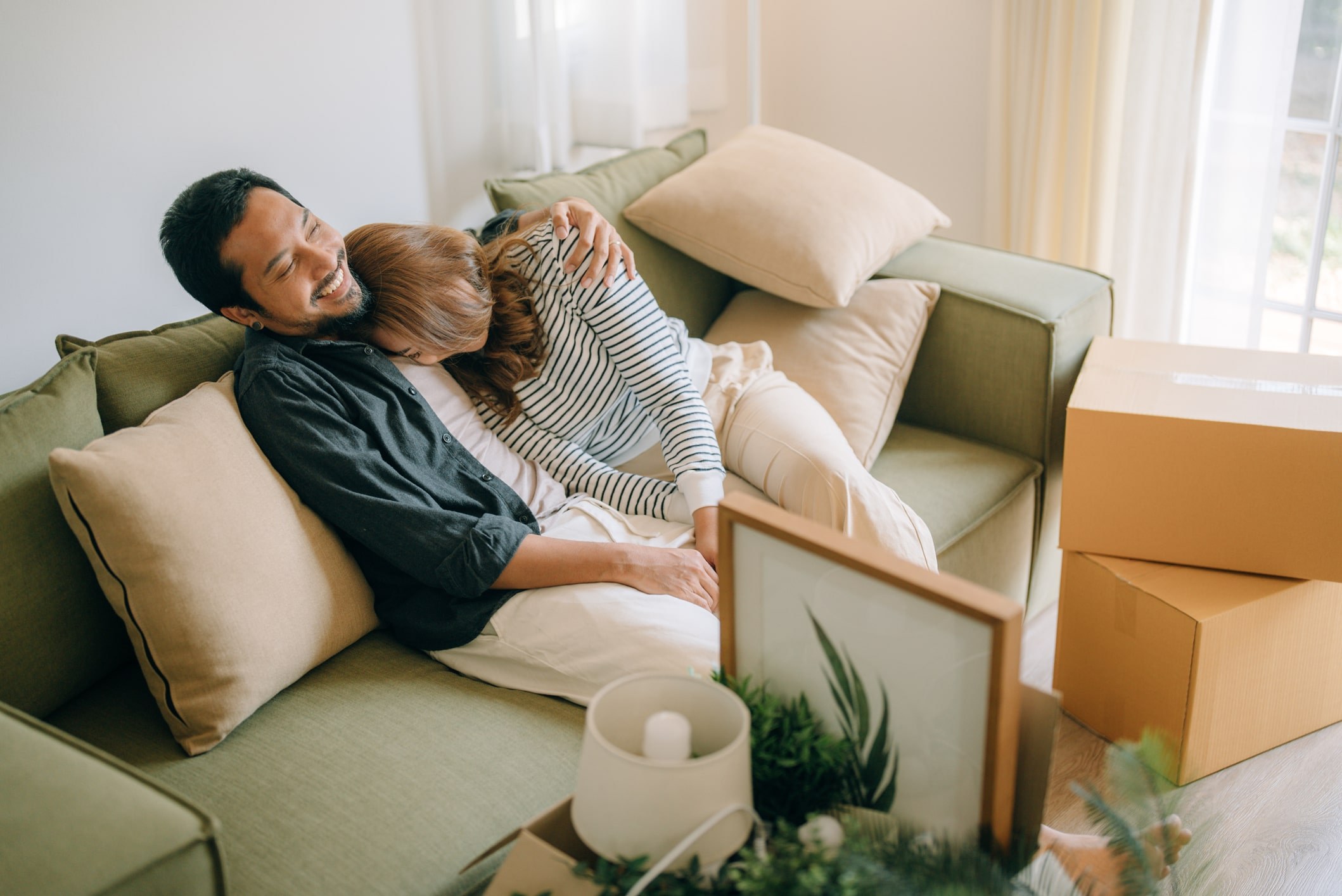 First-time homebuyers sitting on couch, smiling in their new home