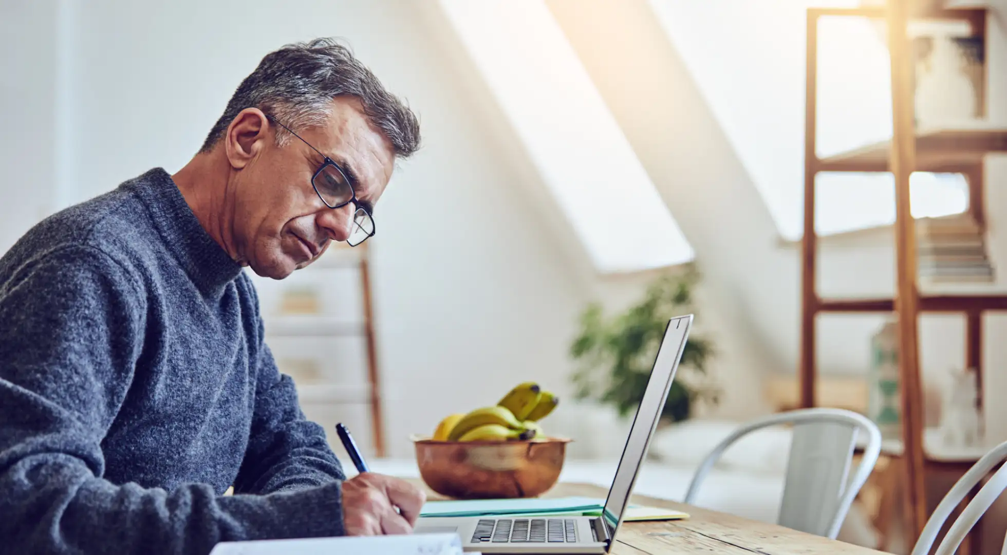 Man researching on his computer and taking notes with a pen and paper.