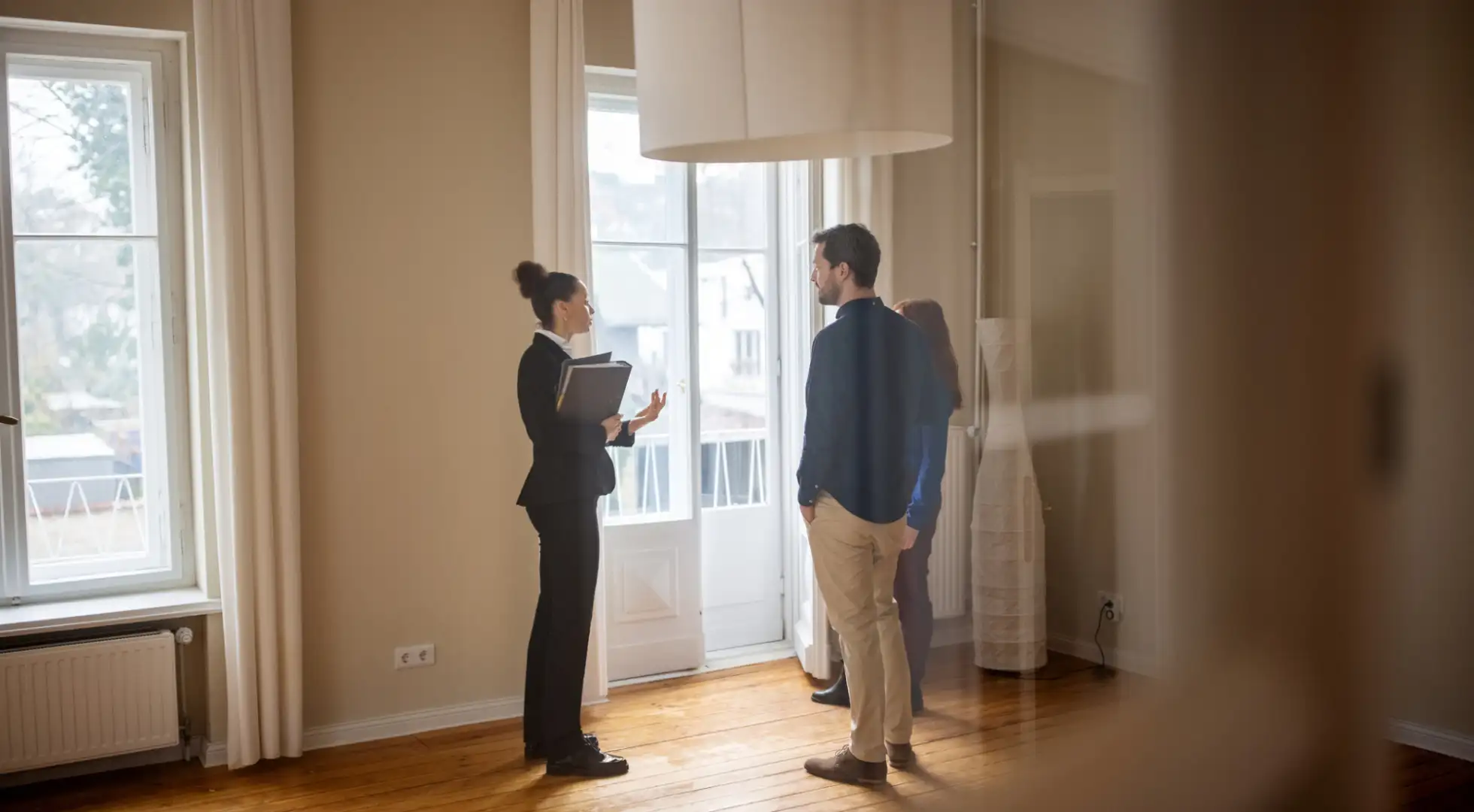 A real estate agent explains FHA repair escrow details to a couple in a spacious, well-lit empty room.