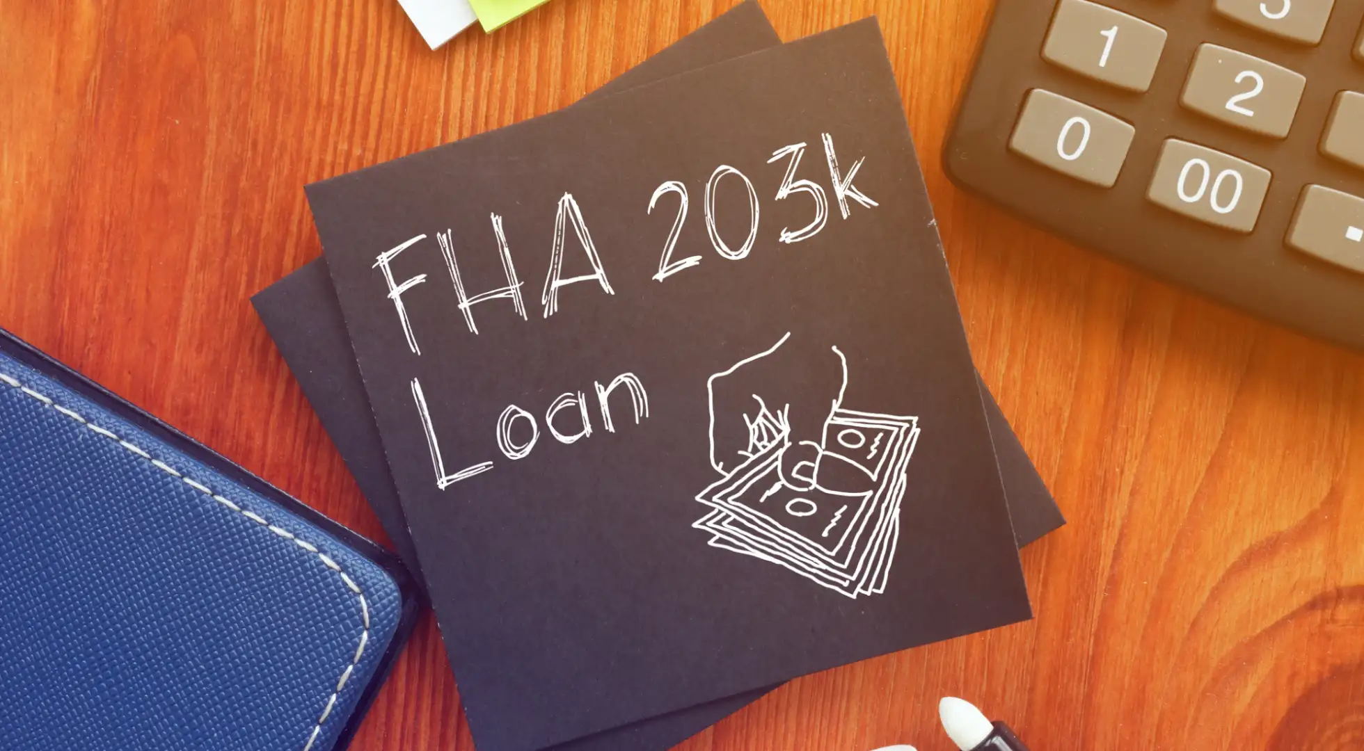 A notepad with "FHA 203k Loan" written on it, alongside drawings of money, on a desk with a calculator and office supplies.