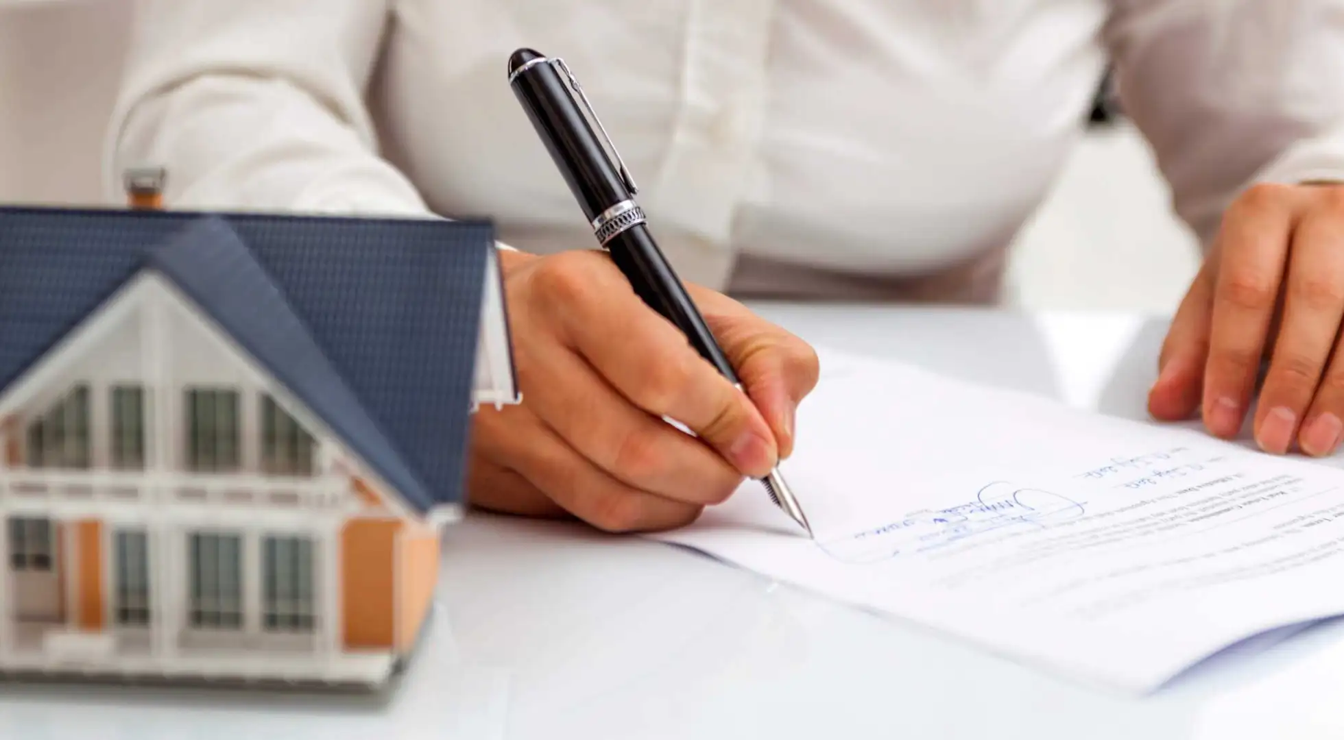 Homeowner signing paperwork next to a small house sitting on desk