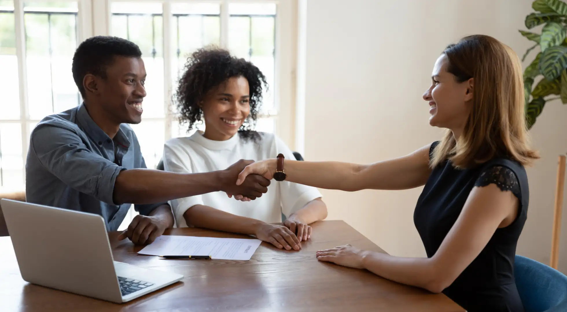 a couple with a contract in front of them shaking hands with their real estate agent