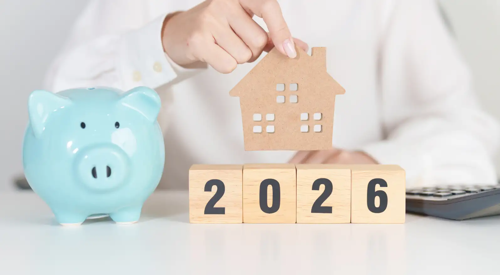 cut-out of a home over blocks reading 2026 and a blue piggy bank