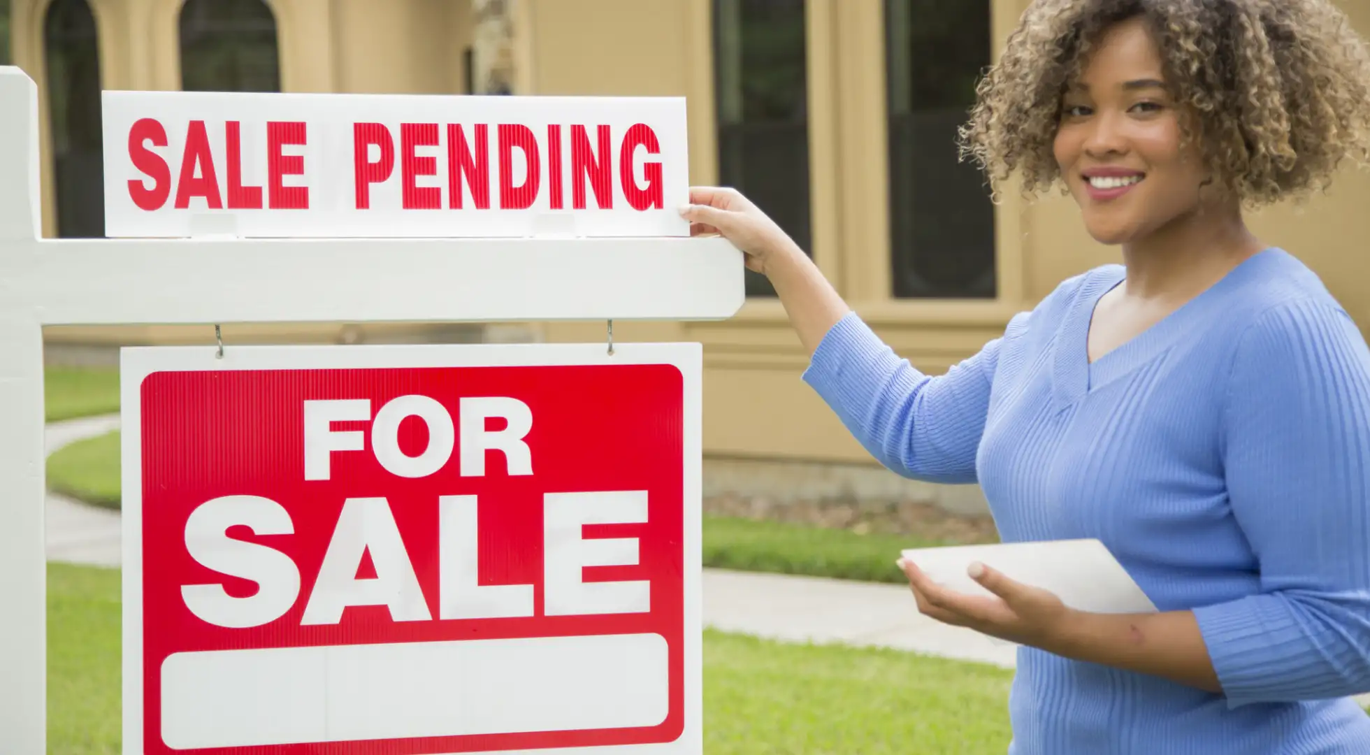 real estate agent standing next to a for sale sign with a rider reading sale pending