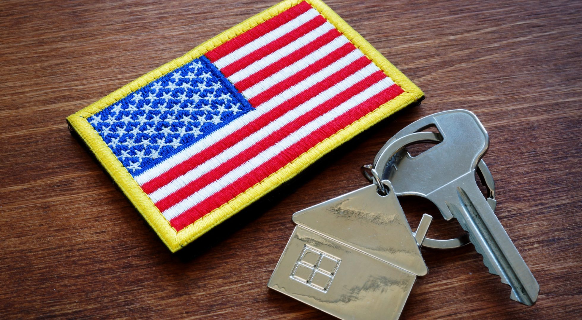 A house key lies on a table next to a military patch shaped like an American flag.