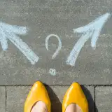 Person wearing yellow shoes standing near two arrows and a question mark drawn on the pavement, indicating a decision point.