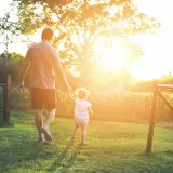 Man and daughter walk around field during sunset