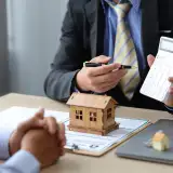 What's The Real Deal on Down Payments: How Much Do I Need to Buy a House? Person holding a calculator next to the model of a house.