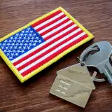 A house key lies on a table next to a military patch shaped like an American flag.